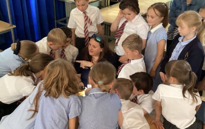 Dr Fay Couceiro looking through a microscope surrounded by a group of children