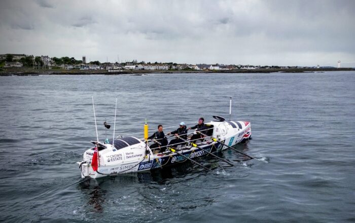 An ocean rowing boat with three rowers on the sea.