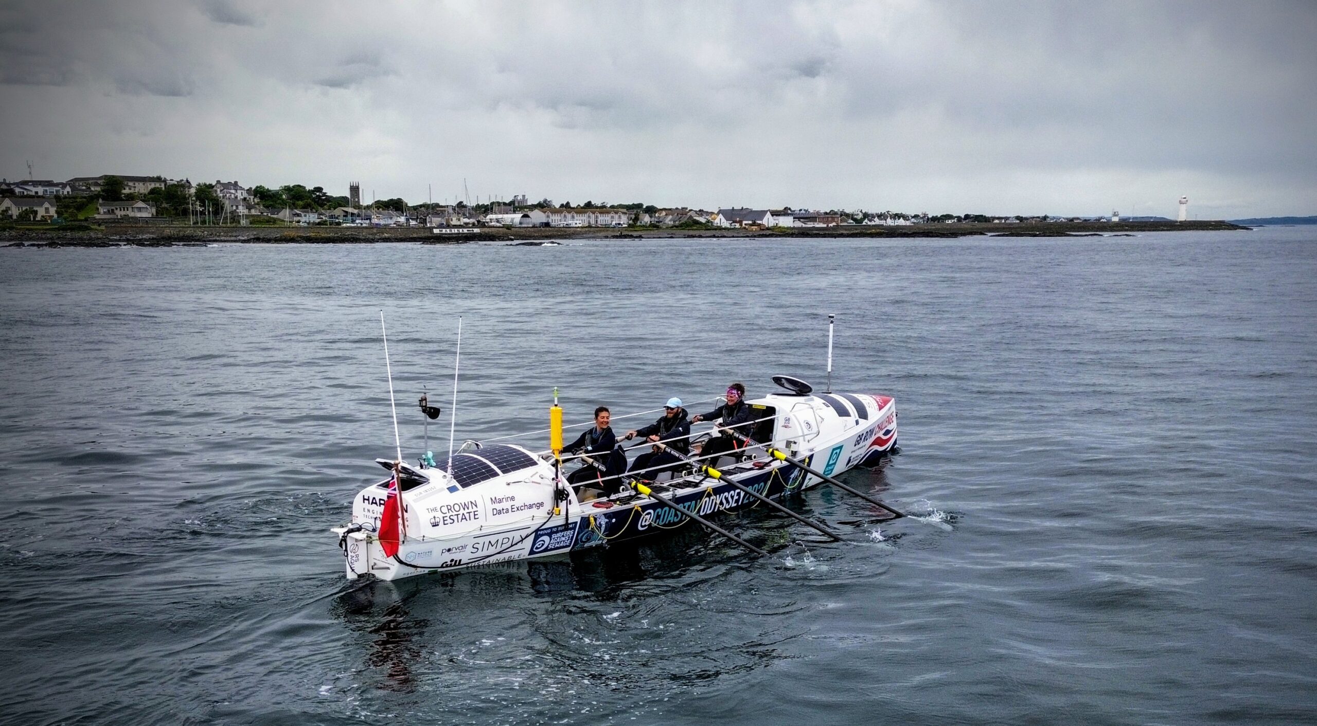 An ocean rowing boat with three rowers on the sea.